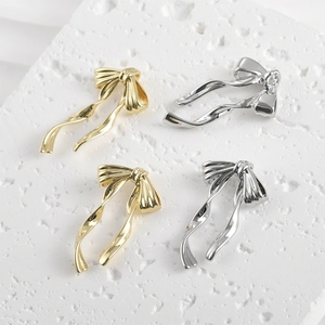 Polished 14k gold and silver bow-knot charms on a minimalist stone background