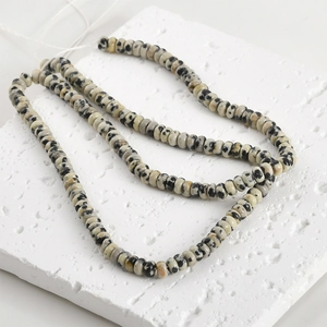 Detailed view of natural Dalmatian Jasper flat beads on a textured plaster display board