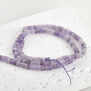 Close-up of translucent purple jade abacus beads on a textured white display board