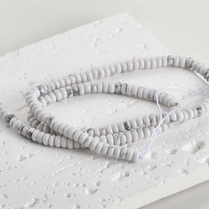 Close-up of natural white turquoise disc beads with grey marble texture on a stone plate