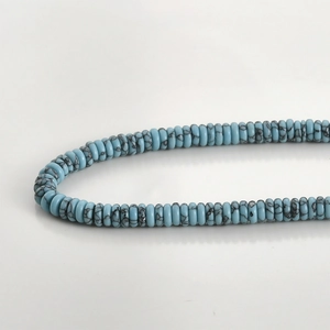 Macro detail of light blue heishi beads with black marble veins on a clean gray background