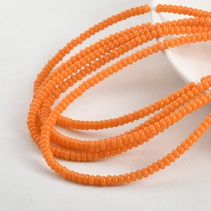 Macro shot of 2x4mm bright orange glass beads draped on a white ceramic bowl for DIY