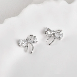 Macro detail of silver bow earrings with pear-cut zircon and streamlined metal ribbons