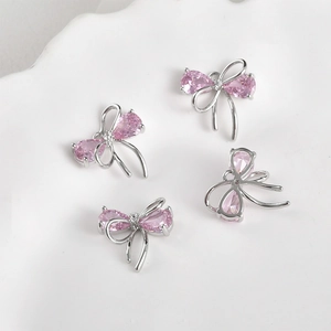 Detail of four 14k gold-plated bow pendants with pink zircon stones on a ceramic tray