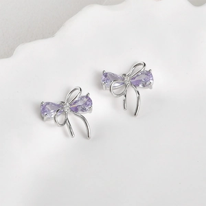 Macro shot of silver bow earrings with purple drop-shaped cubic zirconia and fine diamonds