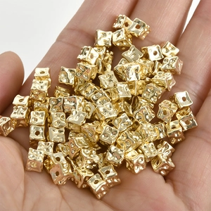 Macro shot of 14k gold-plated textured square beads for DIY jewelry making in palm