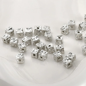 Macro detail of silver hammered cube spacer beads for DIY jewelry making on white ceramic