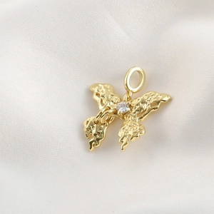 Macro detail of gold butterfly pendant with lava texture and tiny zircon on white silk
