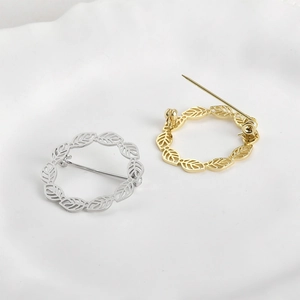 Detaillierte Makroansicht der 14k Gold und Silber Blattkranz-Broschen auf weißer Keramik