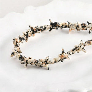 Detailed view of spotted starfish beads for DIY jewelry on a white ceramic tray