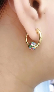 Polished gold hoop earrings with a colorful pave zircon ball pendant on model ear