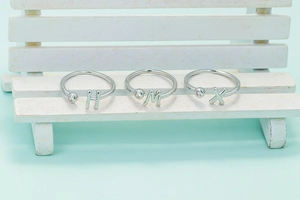 Vista macro de anillos abiertos de plata con letras H, M, X y pequeñas piedras de circón
