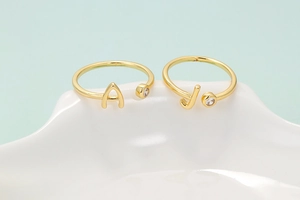 Detalle de anillos dorados ajustables con letras A y J y piedras de circonita brillante