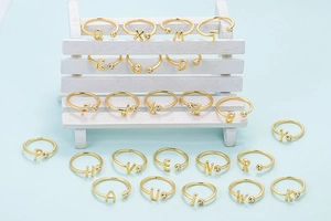 Detalle de anillo ajustable dorado con circonita y colgantes de letras del alfabeto