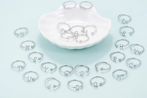 Detalle de anillos plateados ajustables con letra y cuenta en una bandeja de concha