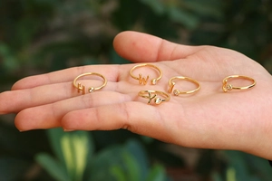 Vista detallada de anillos ajustables bañados en oro con letras y circonitas en una mano
