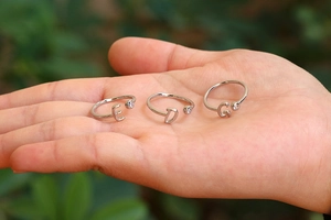 Detalle de anillos plateados con letras y circonitas brillantes mostrados en la mano