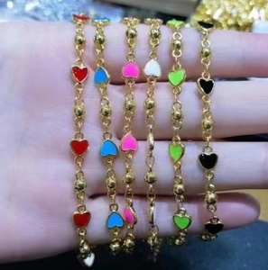 Détail de breloques coeurs en émail coloré sur de fins bracelets en perles dorées en six tons