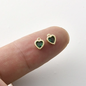 14k gold plated heart charm with green zircon crystal shown on fingertip for size reference