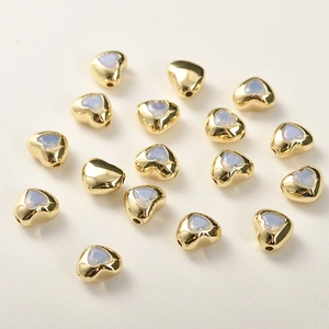 Dettaglio macro di perline a cuore placcate in oro con zirconi per gioielli fai da te