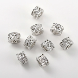 Close-up of silver charms with pavé cubic zirconia and镂空 floral patterns on white background