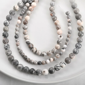 Macro shot of natural stone beads with grey marble texture and ink patterns on a ceramic tray