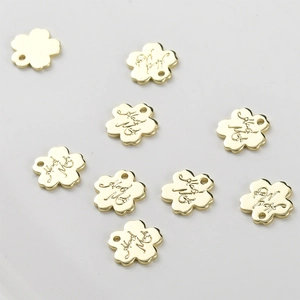 Macro detail of 14k gold-plated floral charms featuring engraved Hand Made text for DIY