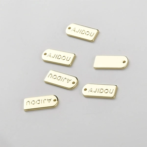 Detail showing 14k gold-plated rectangular jewelry tags with AJIDOU engraving and small hanging holes
