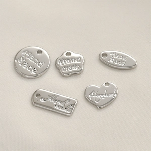 Nahaufnahme diverser silberner Handmade-Metallanhänger für DIY-Schmuck auf Stoff