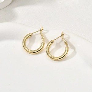 Boucles d'oreilles créoles dorées à l'or 14 carats sur un plateau en céramique blanc