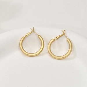 Détail de boucles d'oreilles créoles dorées mat avec fermoir charnière sur support