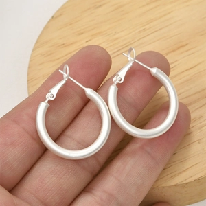 Vue détaillée de créoles rondes en argent mat tenues devant un fond en bois