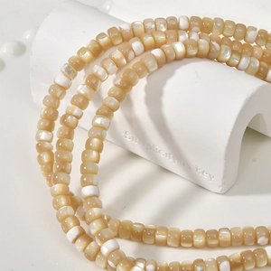 Macro shot of 3x5mm natural mother of pearl wheel beads on a minimalist white stand