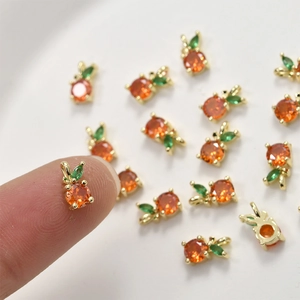 Macro shot of 14k gold plated orange zircon fruit charm on a fingertip for DIY jewelry