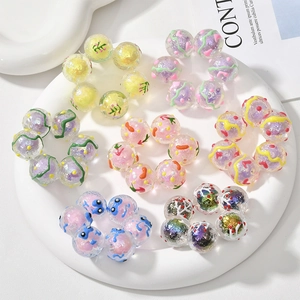 Nahaufnahme bunter Acrylperlen mit Glitzer und Blumenmustern in einer Keramikschale