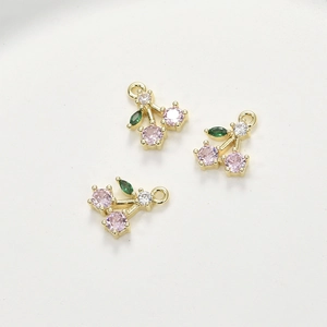 Detailed macro view of cherry fruit charms with pink and green zircon stones on gold base