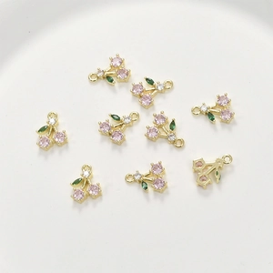 Macro view of cherry-shaped gold pendants with pink and green zircon stone settings