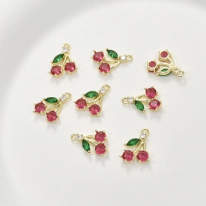 Macro detail of cherry-shaped gold pendants with red and green zircons for DIY jewelry