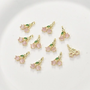 Macro detail of 14k gold cherry pendants with pink opal beads and green zircon leaves