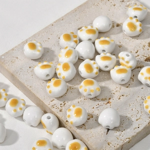 Handmade ceramic cat paw beads with orange details for DIY jewelry on stone tray