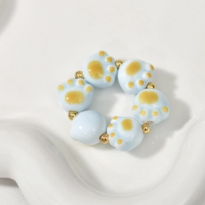 Detailed view of light blue ceramic cat paw beads with gold spacers on a display plate