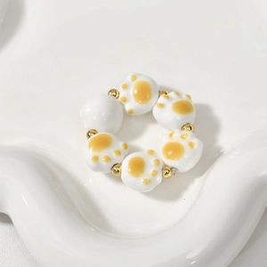 Detailed view of ceramic cat paw beads and golden metal beads on a white tray