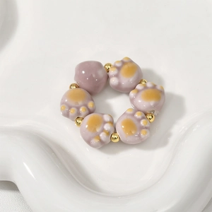 Macro detail of ceramic cat paw beads and golden metal spacers on a wavy tray