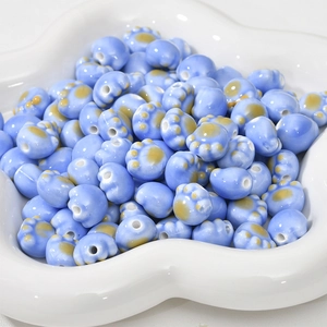 Macro shot of light blue ceramic cat paw beads in a white bowl for DIY jewelry making