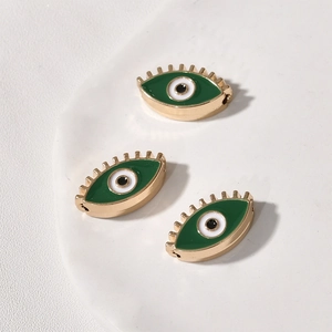 Detail von grünen Evil-Eye-Perlen mit goldenen Wimpern auf einem weißen Tablett
