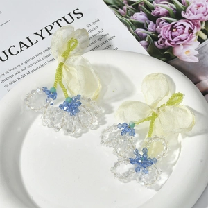Detail of handmade chiffon bow and blue crystal flower bead earrings in a white ceramic dish