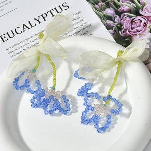 Detail of handmade floral crystal earrings with light yellow organza bow on ceramic tray