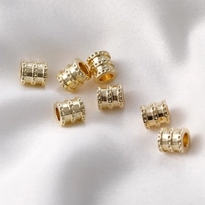 Macro shot of 14k gold-plated barrel beads with dotted texture on white silk fabric