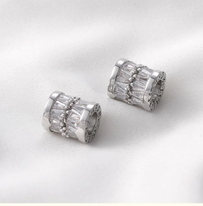 Detailed macro of silver barrel charm with baguette zircons and side letter engraving