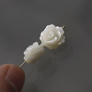 Macro detail of hand-carved white shell rose beads on a gold pin for DIY jewelry
